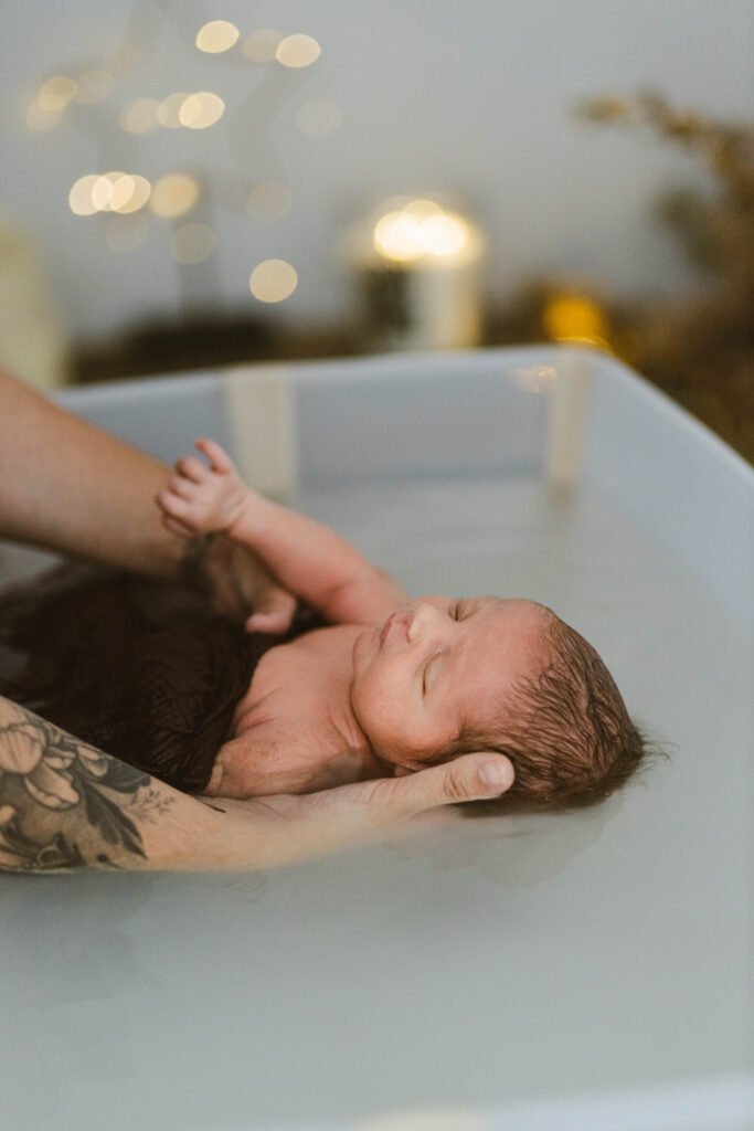 premier bain d'un bébé tenu par ses parents avec des lumières derrière