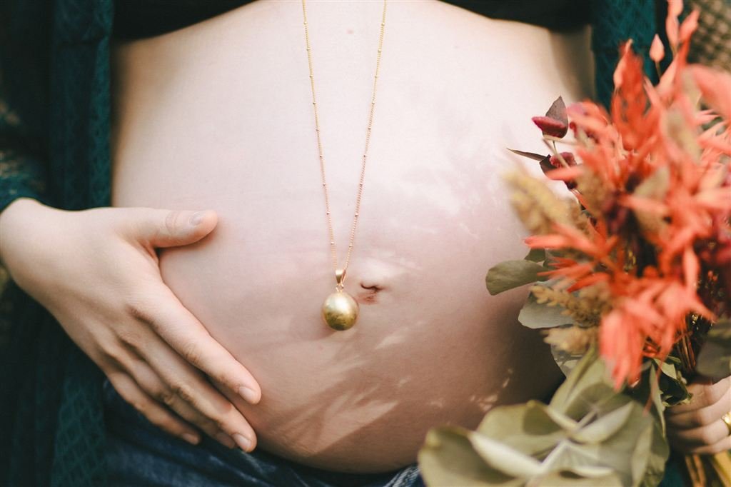 Photo de grossesse : main posée sur un ventre rond, un bola doré et un bouquet de fleurs séchées