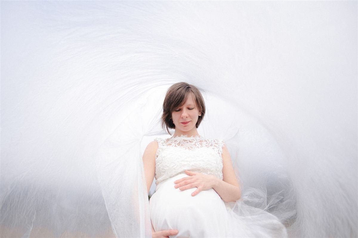 Séance photo grossesse : future maman en robe de dentelle blanche, enveloppée d'un grand voile qui tourbillonne