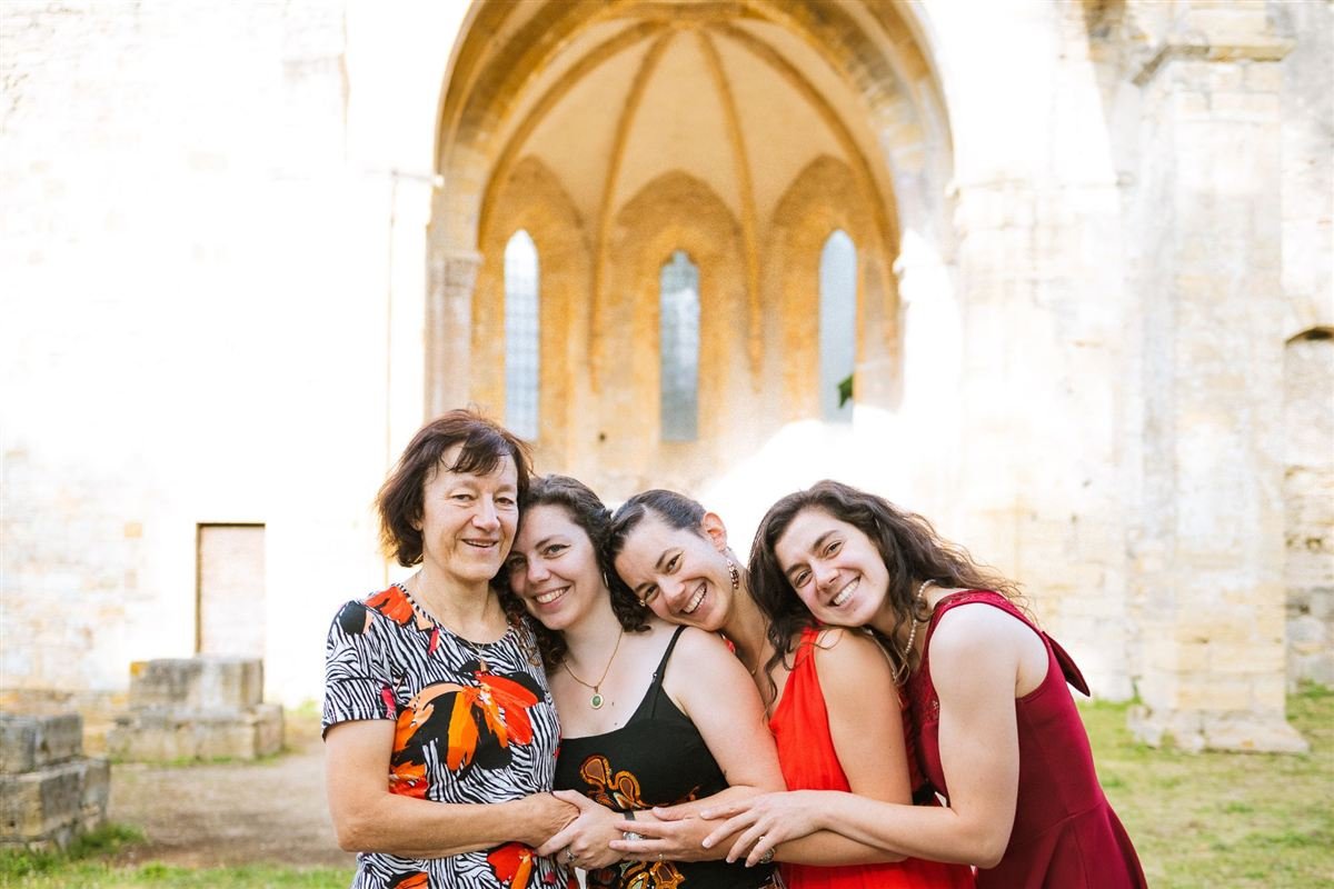Séance photo La Lignée : une mère et ses trois filles enlacées et souriantes devant les ruines d'une abbaye