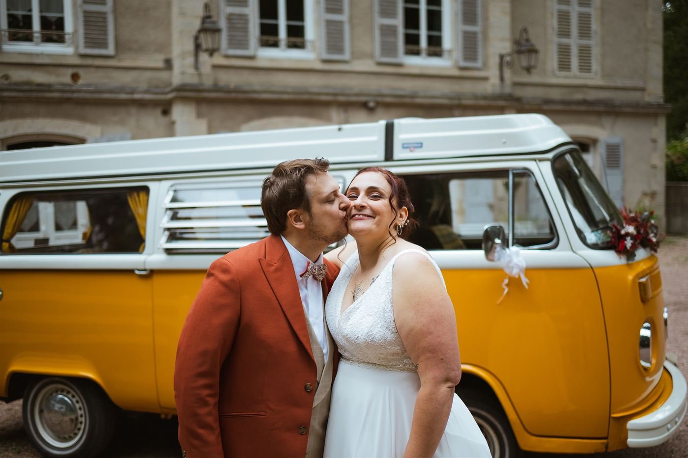 Mariés qui s'embrassent devant un combi Volkswagen jaune le jour du mariage