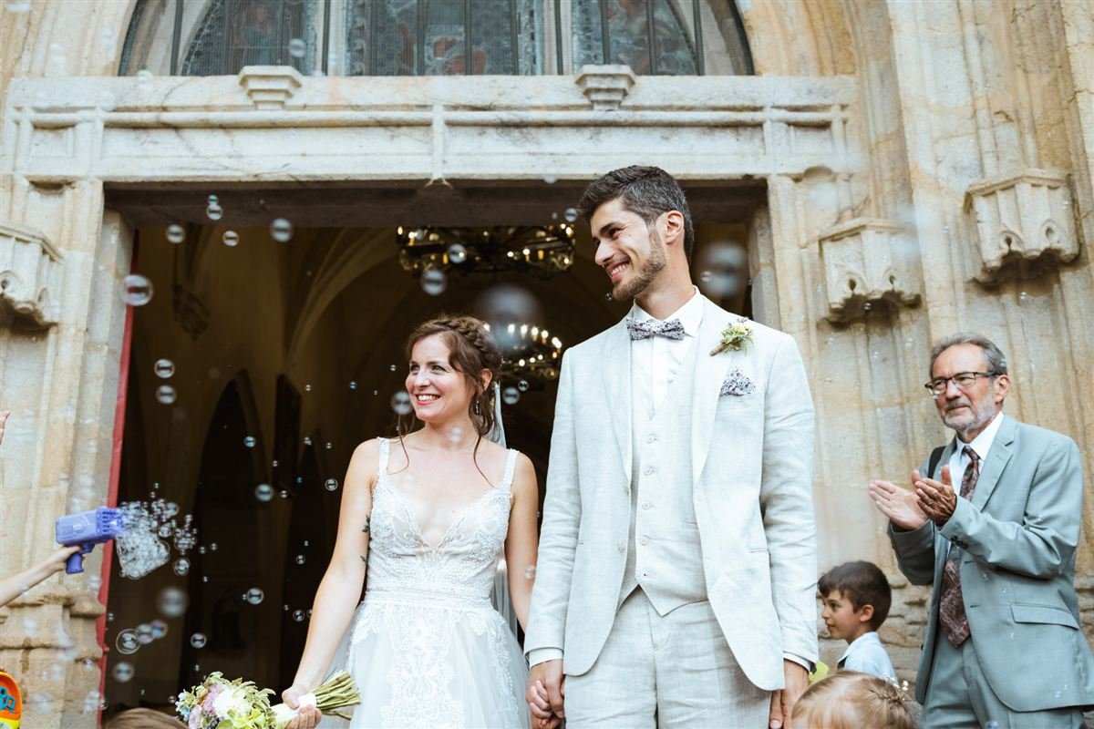 Reportage mariage en Auvergne : les mariés sortent de l'église main dans la main sous les bulles de savon
